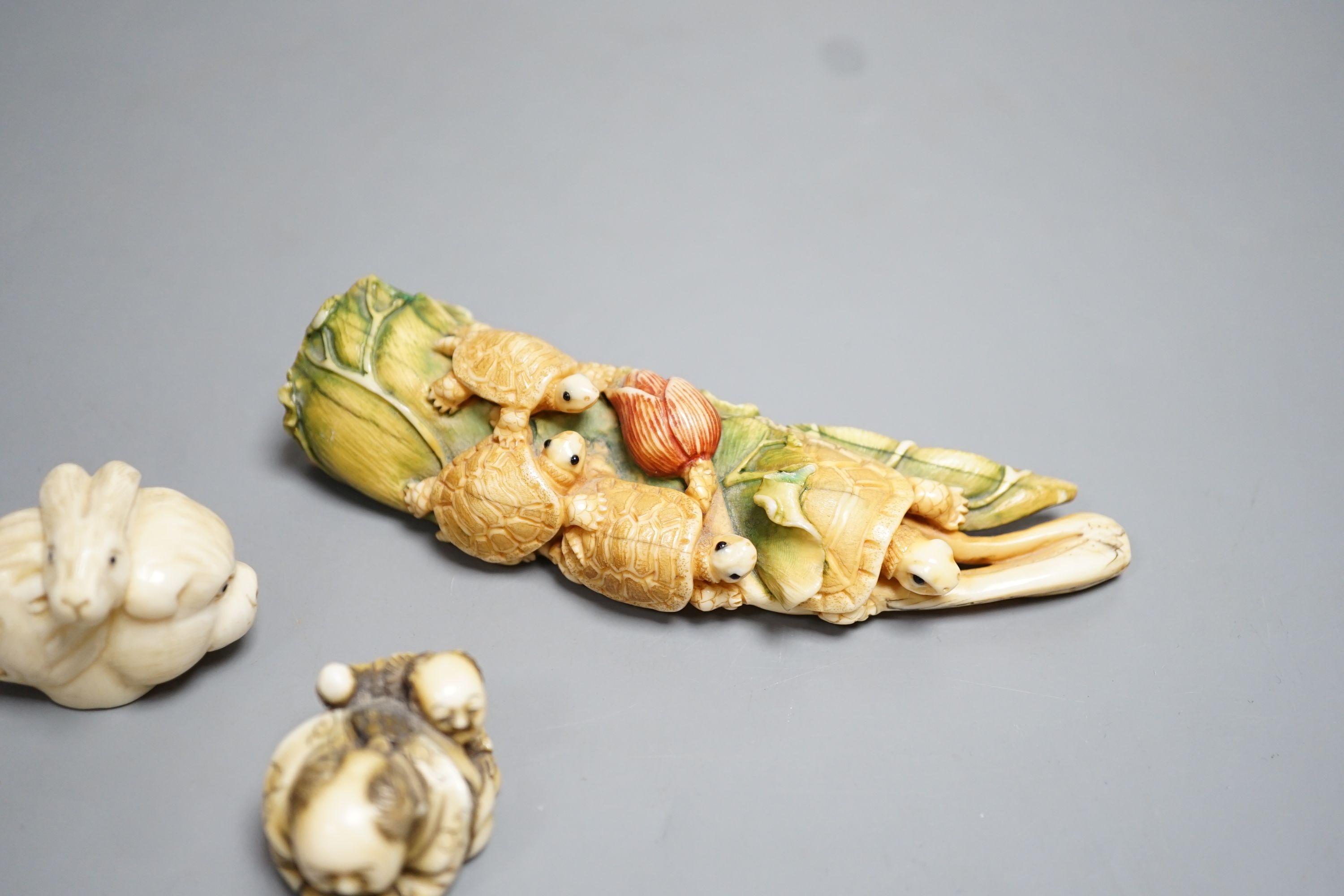 A Japanese ivory Netsuke of two boys holding a noh mask, an ivory Netsuke in the form of three animal heads and a coloured Ivory carving of tortoises on a lotus leaf, all singed (3) largest 12cm